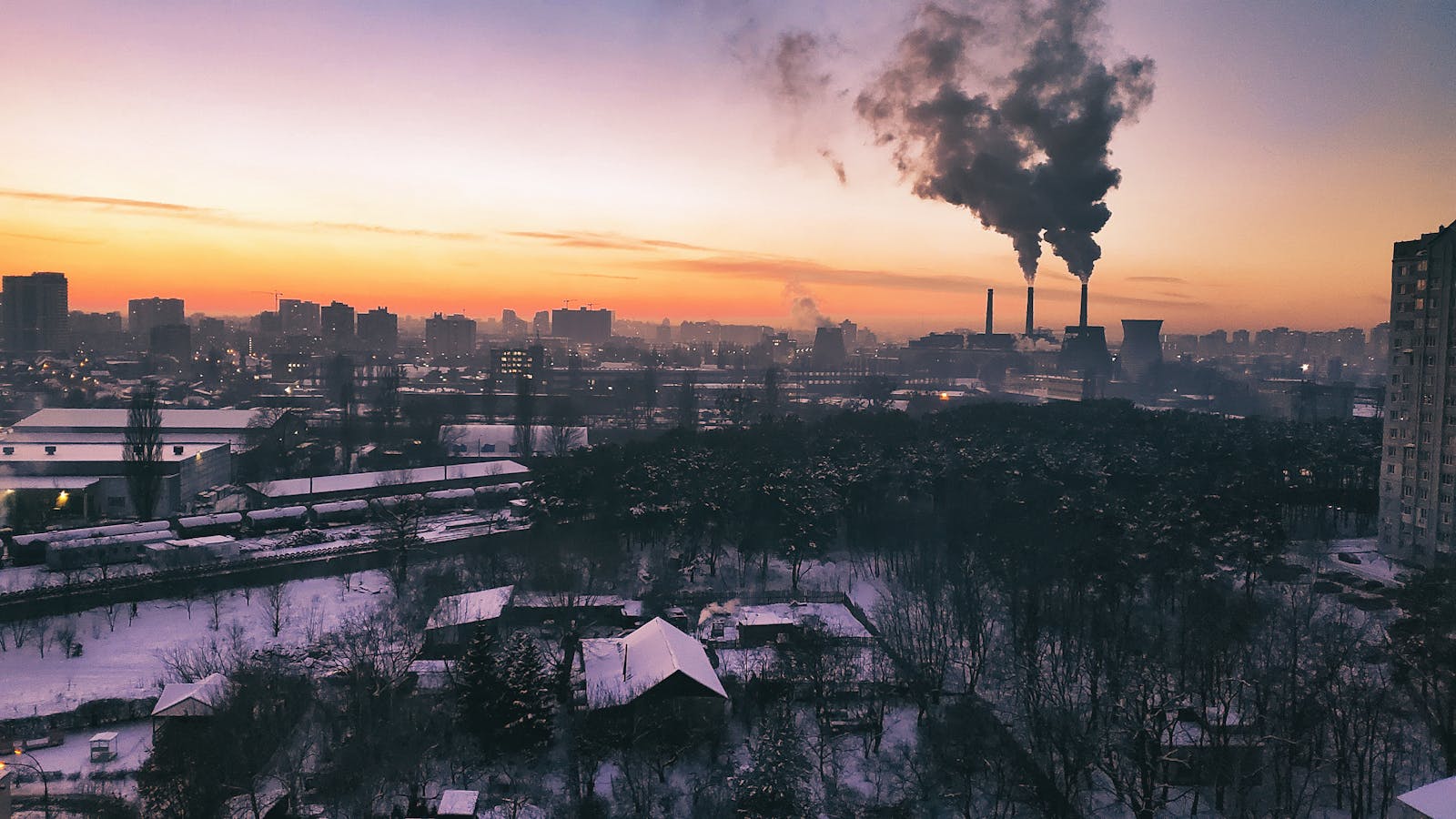 Industrial urban landscape with factory emissions showing nitrogen oxide and pollutant sources that react with volatile organic compounds in sunlight to form ground-level tropospheric ozone damaging plant tissue through reactive oxygen species generation