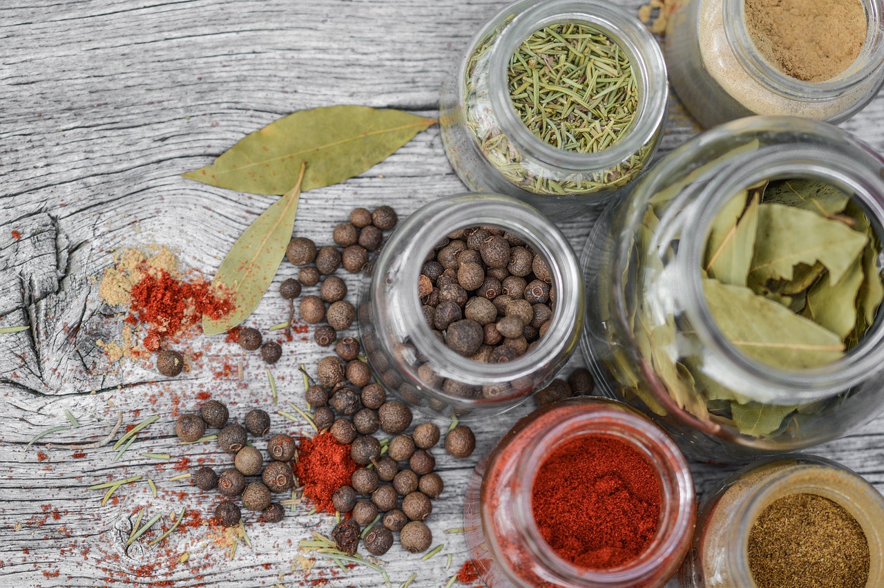 Collection of dried herbs and spices in glass jars including black pepper Piper nigrum rosemary Salvia rosmarinus and bay leaves showing plant secondary metabolite preparations for daily herbal supplement use