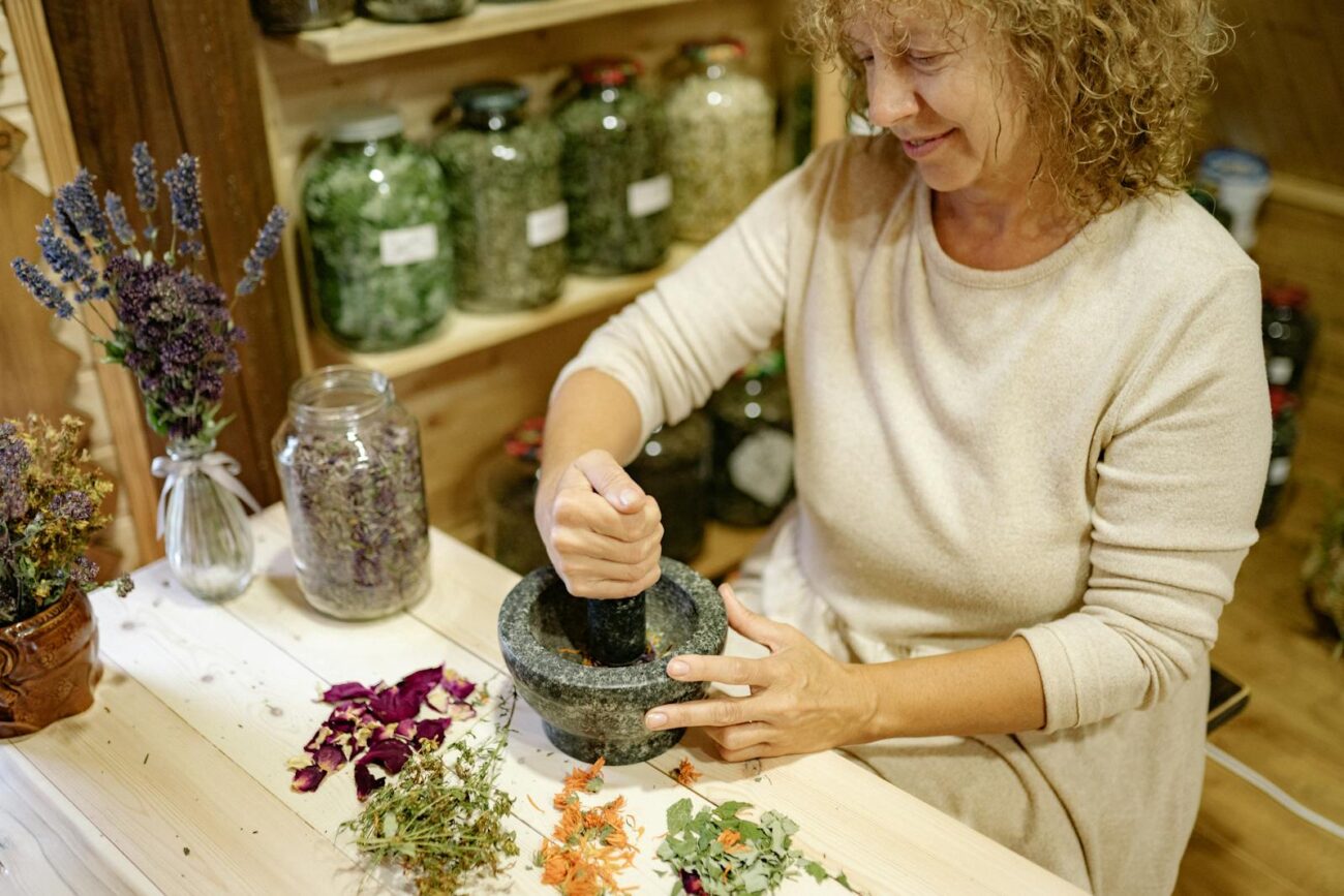 Herbalist grinding dried medicinal plants including lavender calendula and rose petals in mortar and pestle showing traditional herbal remedy preparation with diverse plant secondary metabolite compounds