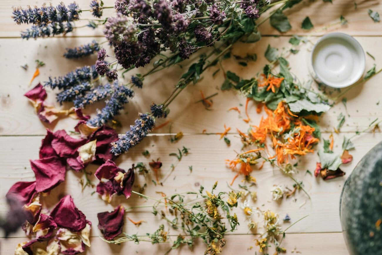Diverse dried medicinal herbs including lavender rose petals and calendula spread on wooden surface showing the range of plant secondary metabolites including monoterpenoids flavonoids and phenolic compounds supporting energy stress sleep and cardiovascular function