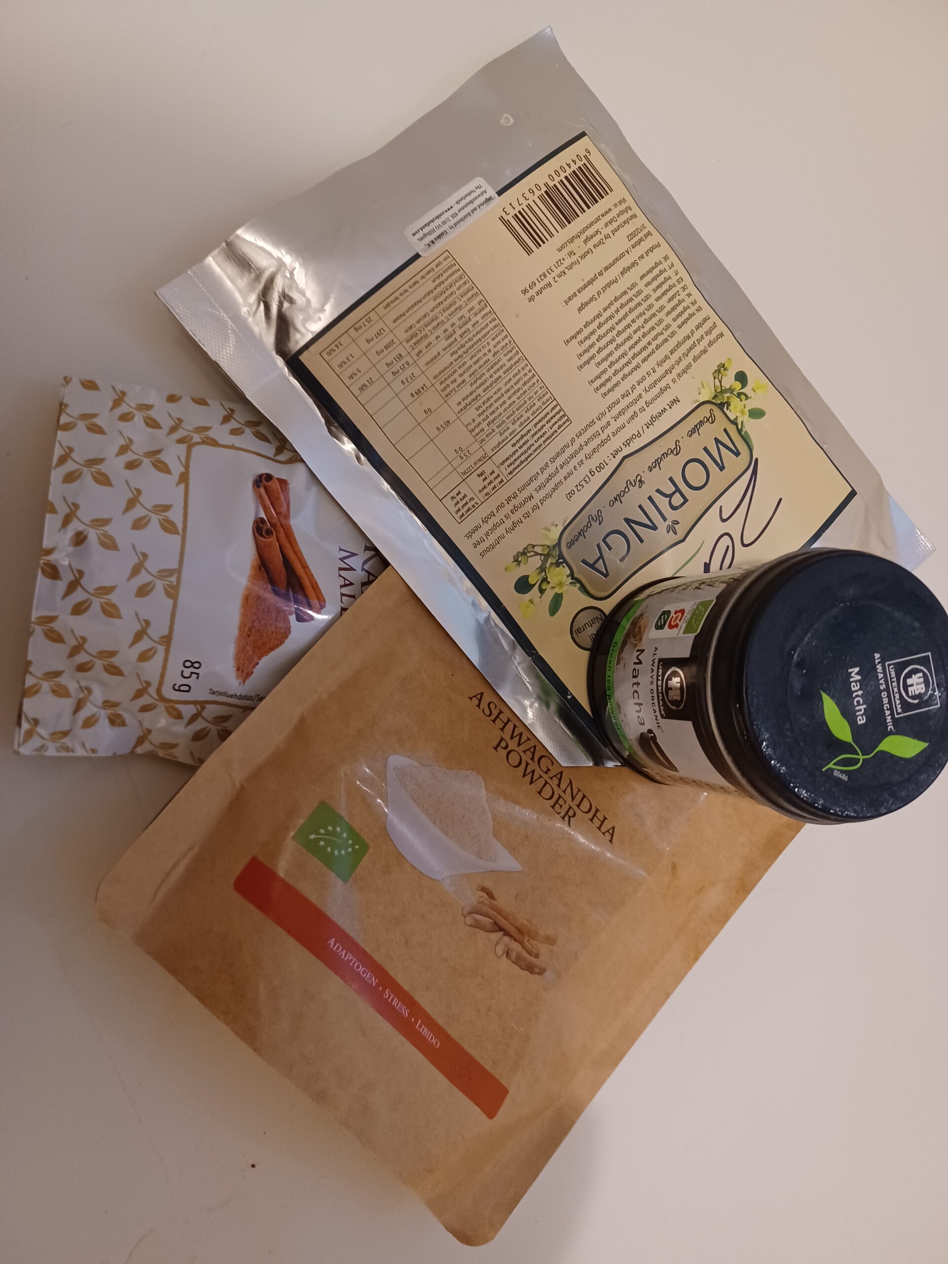 Withania somnifera ashwagandha Cinnamomum verum cinnamon Moringa oleifera and Camellia sinensis matcha personal herbal powder collection on kitchen table showing plant secondary metabolite rich preparations used regularly in daily nutrition by plant biochemist and environmental scientist.