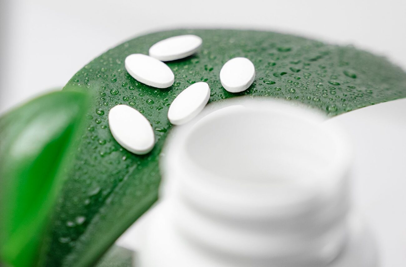 White tablets resting on a green leaf with water droplets beside a bottle.
