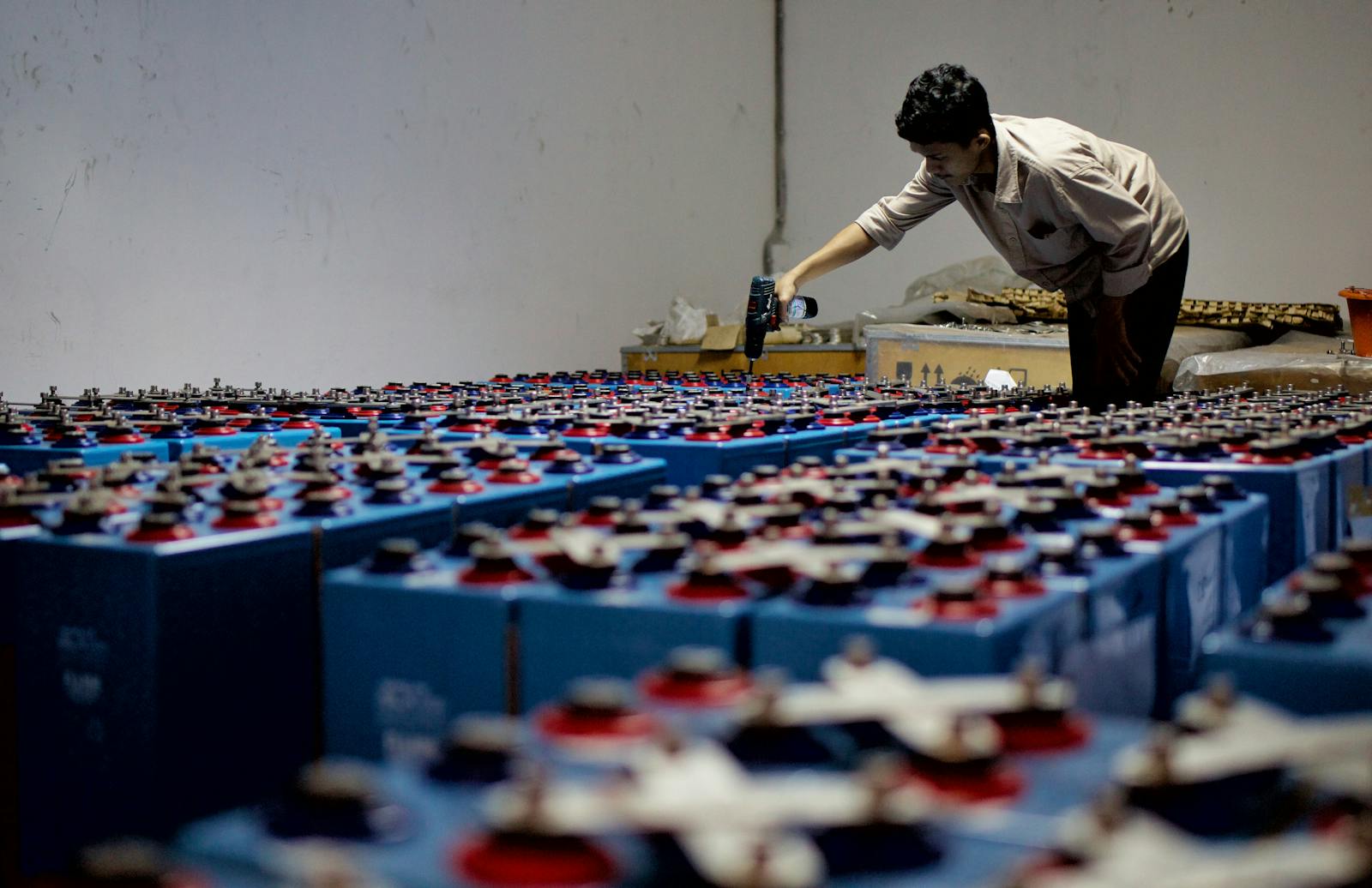 A worker maintaining rows of industrial batteries in a large warehouse showing the scale of battery production and use