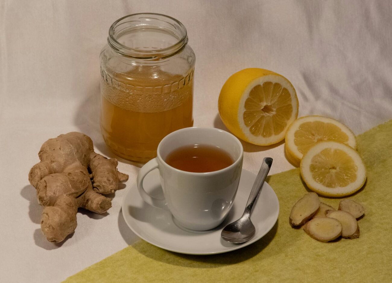 Zingiber officinale fresh ginger root with brewed ginger tea cup and sliced lemon showing gingerol pungent phenolic compound extraction in hot water preparation for digestive support with documented gastric emptying acceleration and gut wall anti-inflammatory activity