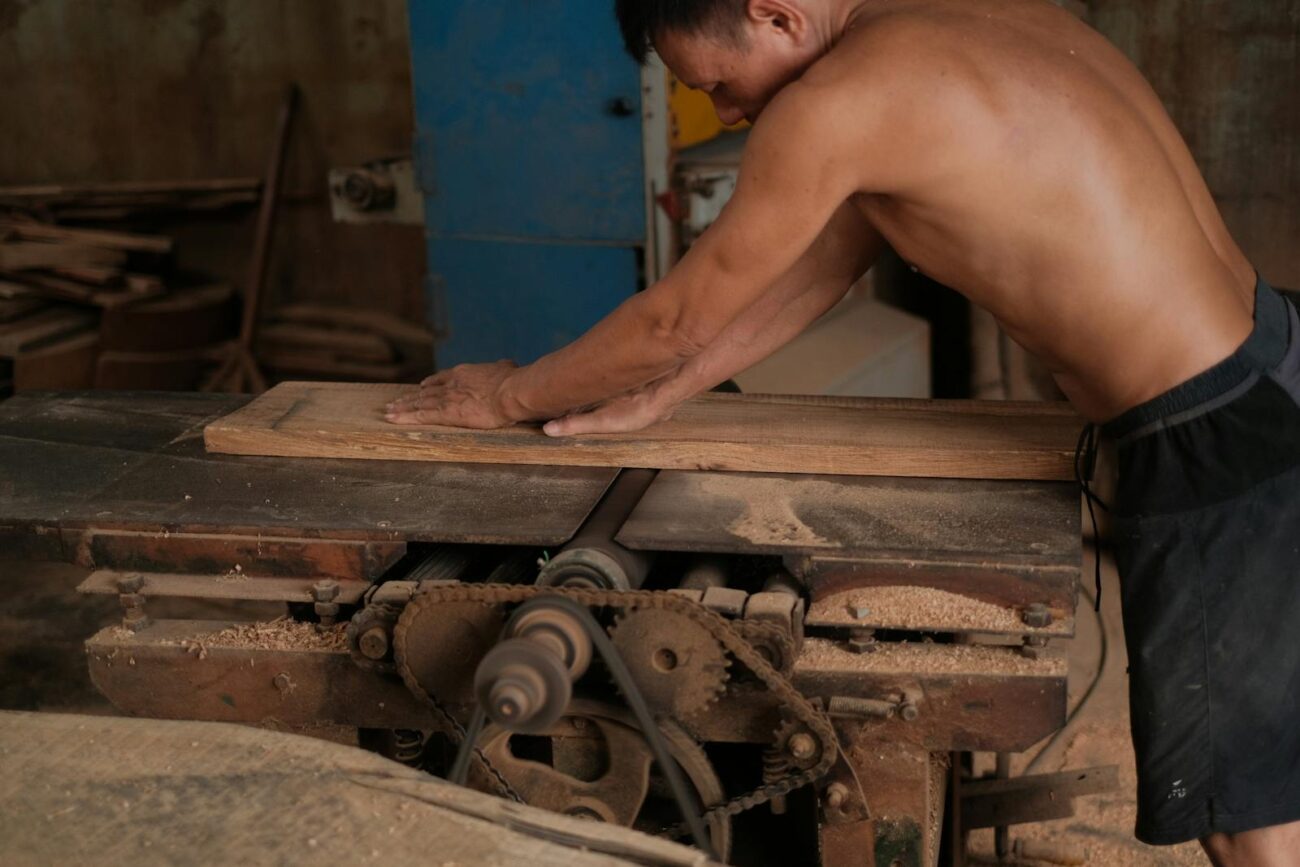 A worker processing a timber plank through a sawmill machine showing wood being worked and given value through skilled craftsmanship