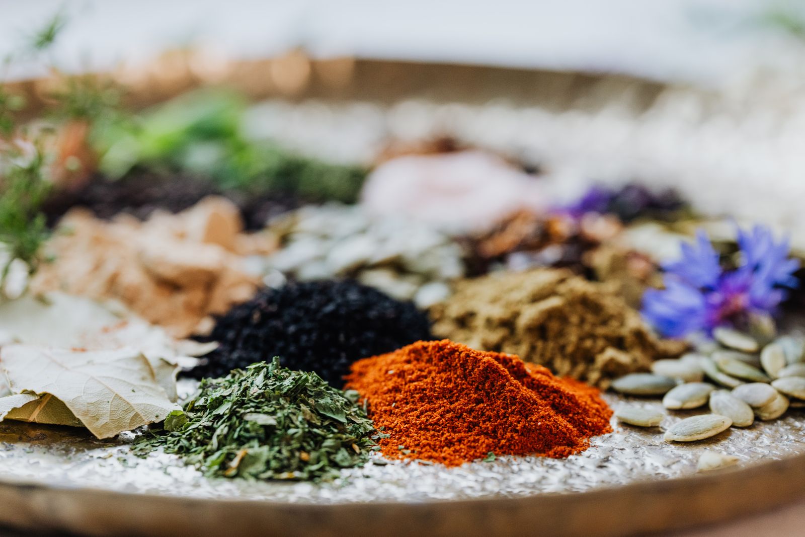 An assortment of dried herbs, spices, and seeds in different colours on a tray