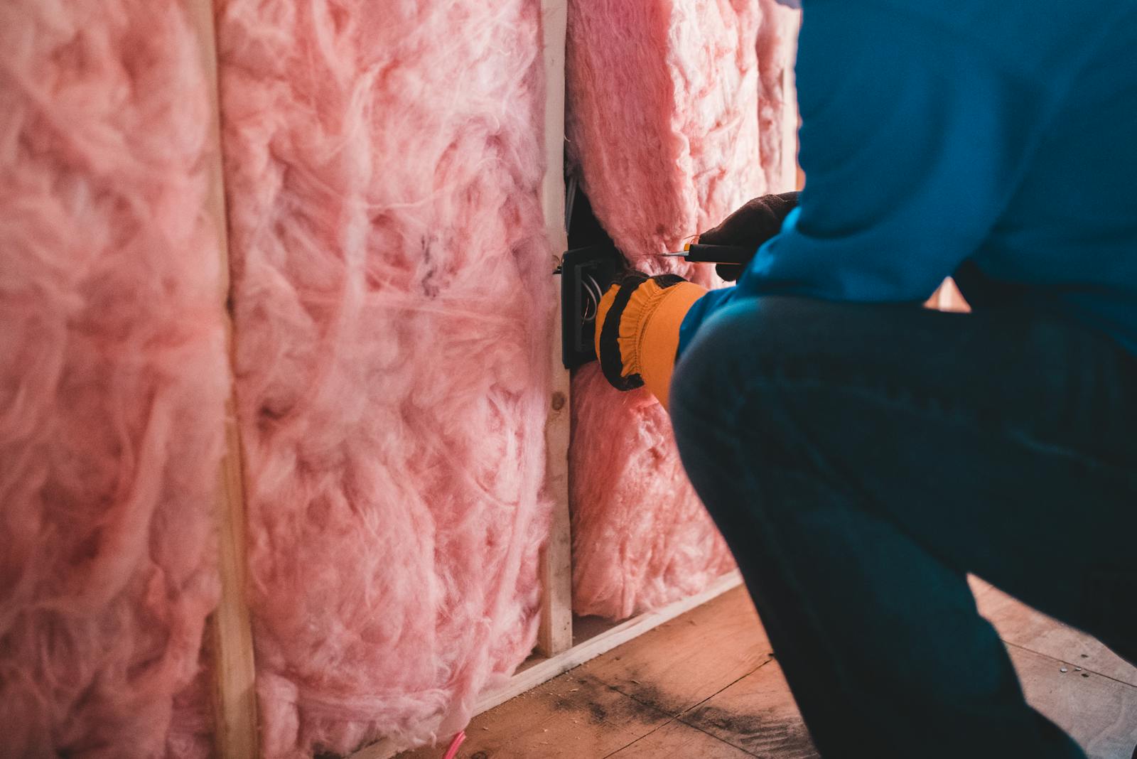 A worker installing pink mineral wool insulation between wall studs to reduce heat conduction in an energy efficient home