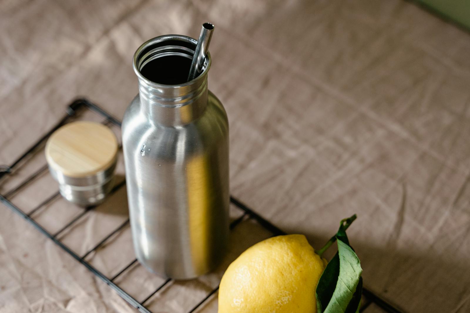 A stainless steel water bottle with metal straw and small container beside a lemon showing BPA and phthalate free alternatives to plastic bottles