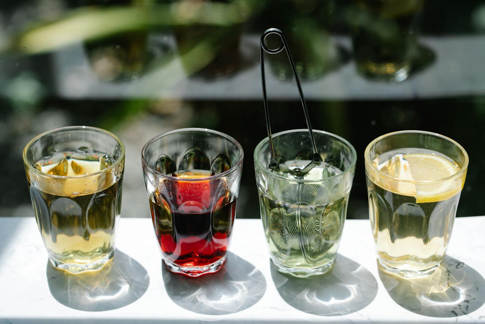 Four glasses of tea in a row showing different colours from pale gold to deep red.