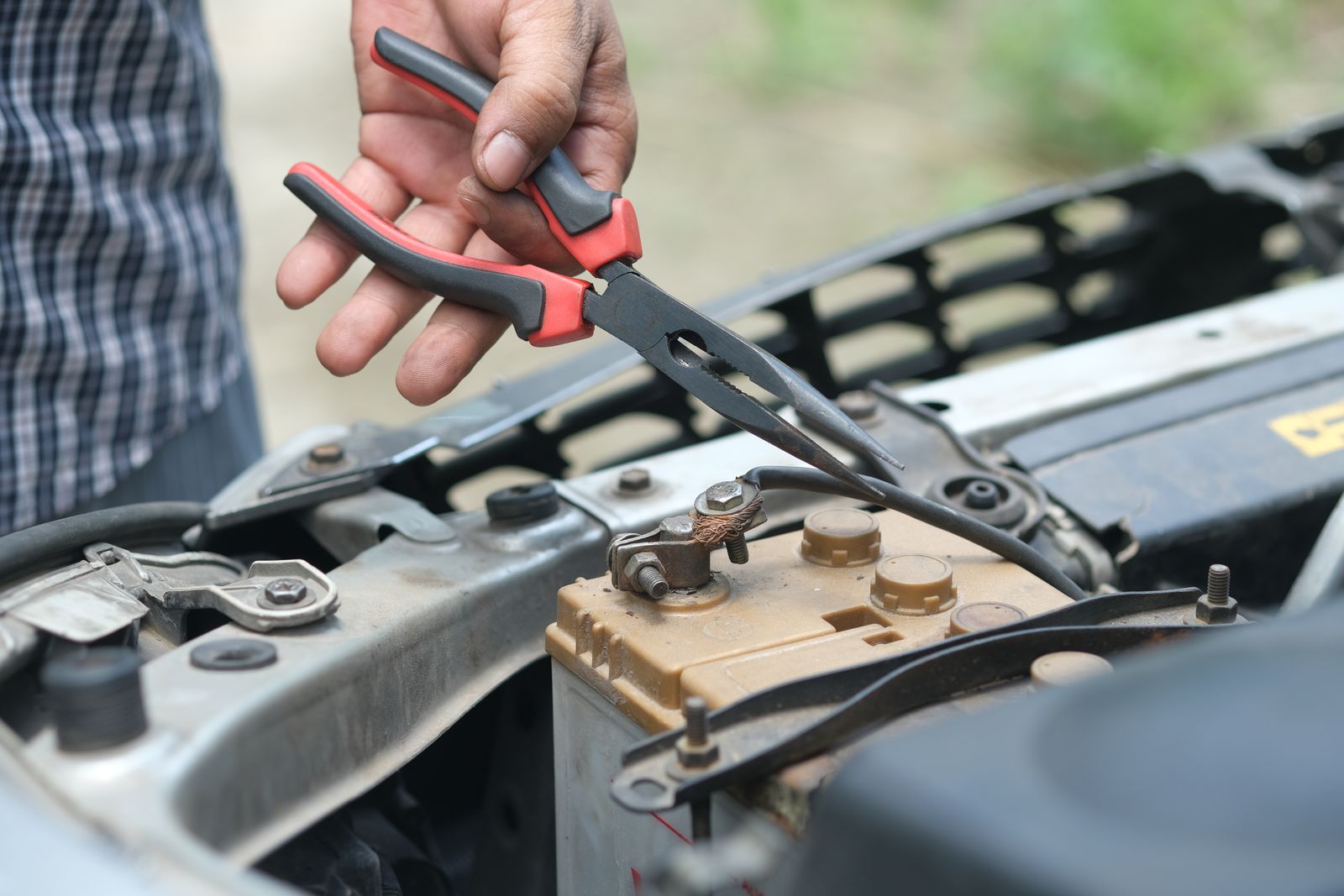 A hand using pliers to work on a corroded car battery terminal during battery maintenance and reconditioning