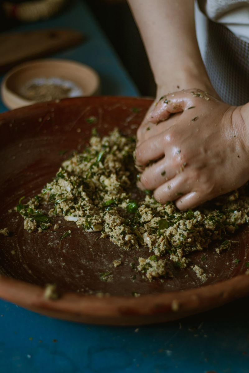 A hand crushing fresh green herbs into a paste in a clay bowl.